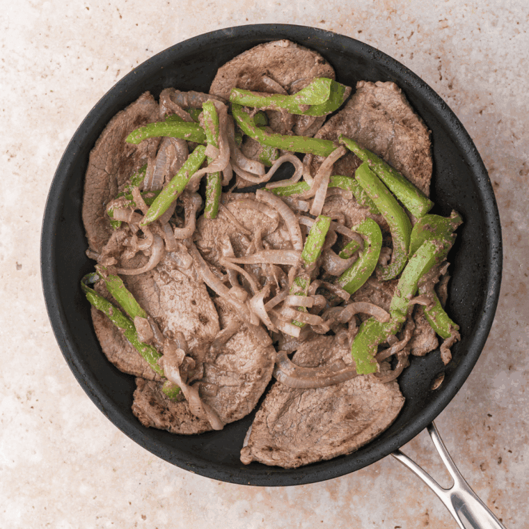 Cooked Easy Ribeye Steak Sandwich with Grilled Onions in skillet.