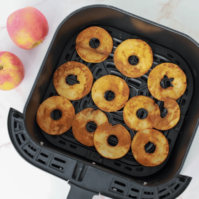 Seasoned apple slices arranged in a single layer inside an air fryer basket for even dehydration.