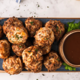 Air Fryer Sausage Balls stacked on a white plate beside a small bowl of spicy maple dipping sauce