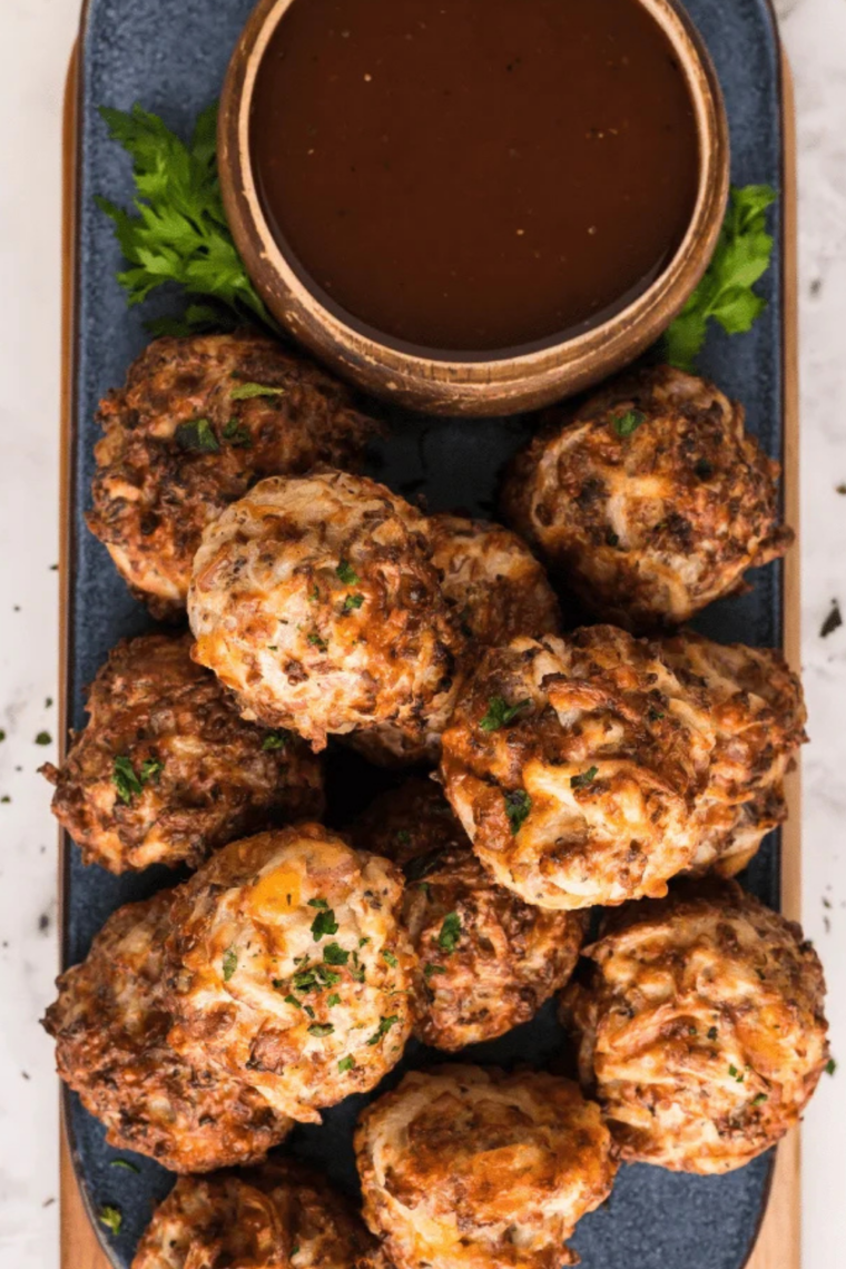 Air Fryer Sausage Balls piled on a white serving plate, golden brown and garnished with chopped parsley