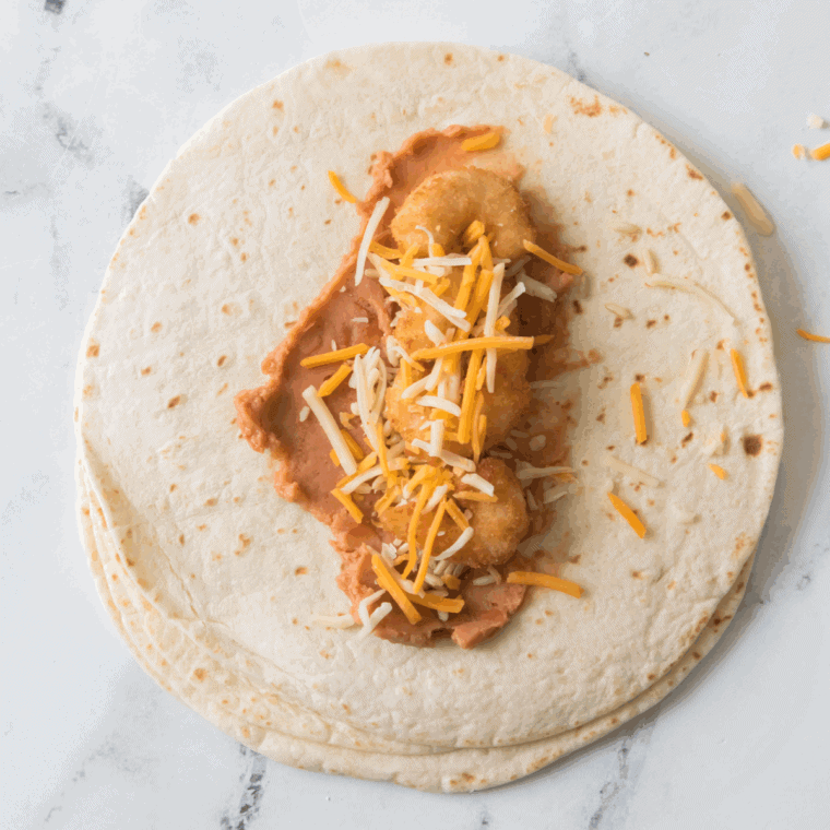 Assembling tortillas with refried beans, rice, shrimp, and cheese in preparation for wrapping.