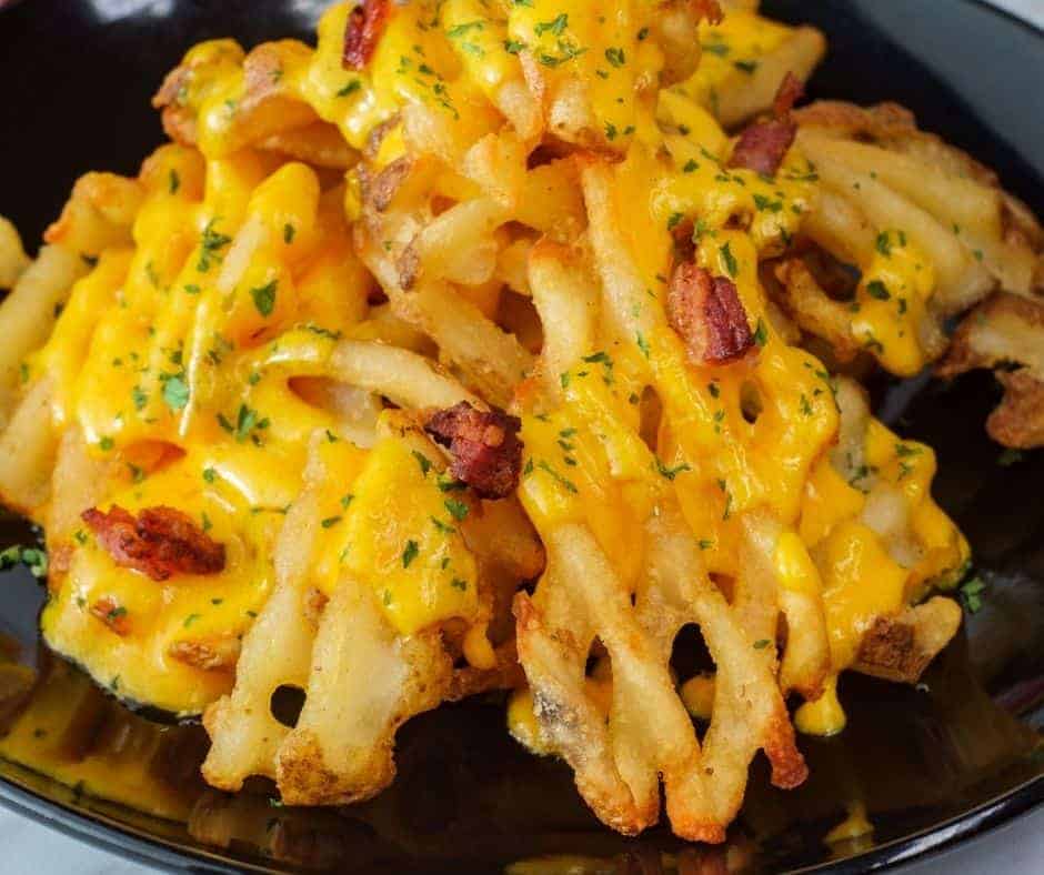 Air fryer waffle fries on a plate with melted cheese and bacon bits.