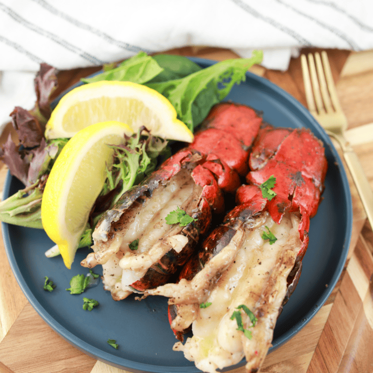 Blackstone Griddle lobster tails cooking on a flat-top grill with garlic butter and fresh lemon wedges.