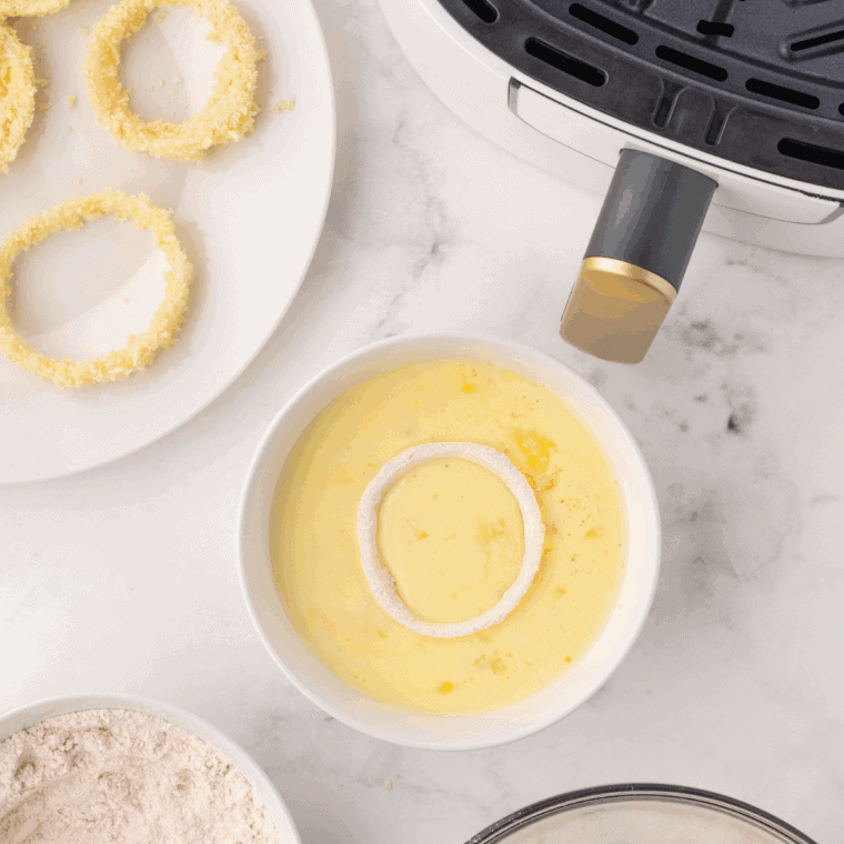 Onion rings soaking in seasoned buttermilk in a bowl.