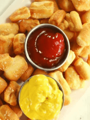 Copycat Culver's pretzel bites piled on a board with a cup of Wisconsin cheddar cheese sauce
