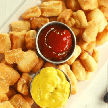 Copycat Culver's pretzel bites piled on a board with a cup of Wisconsin cheddar cheese sauce