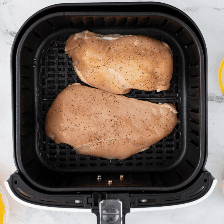 Flipping air fryer chicken and basting with mustard vinaigrette while roasting tomatoes, artichokes, and capers in a saucepan.