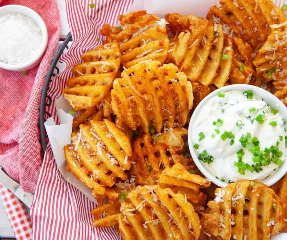Frozen waffle fries in air fryer in a basket with a creamy dip.