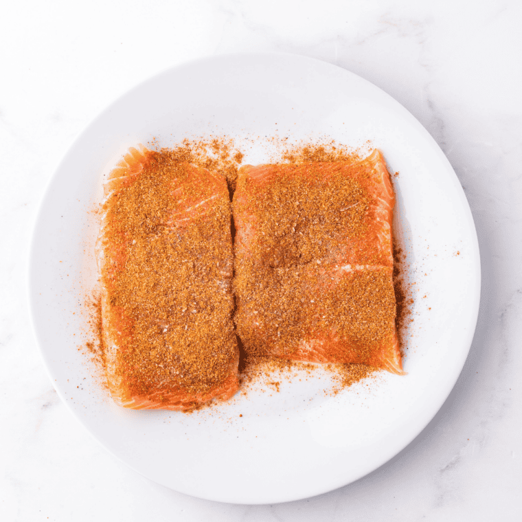 Oil-brushed salmon fillets being coated with Old Bay seasoning rub on the top and sides