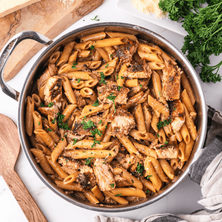 Bowl of creamy Cajun penne pasta tossed in a smoky, spiced sauce and topped with chopped parsley