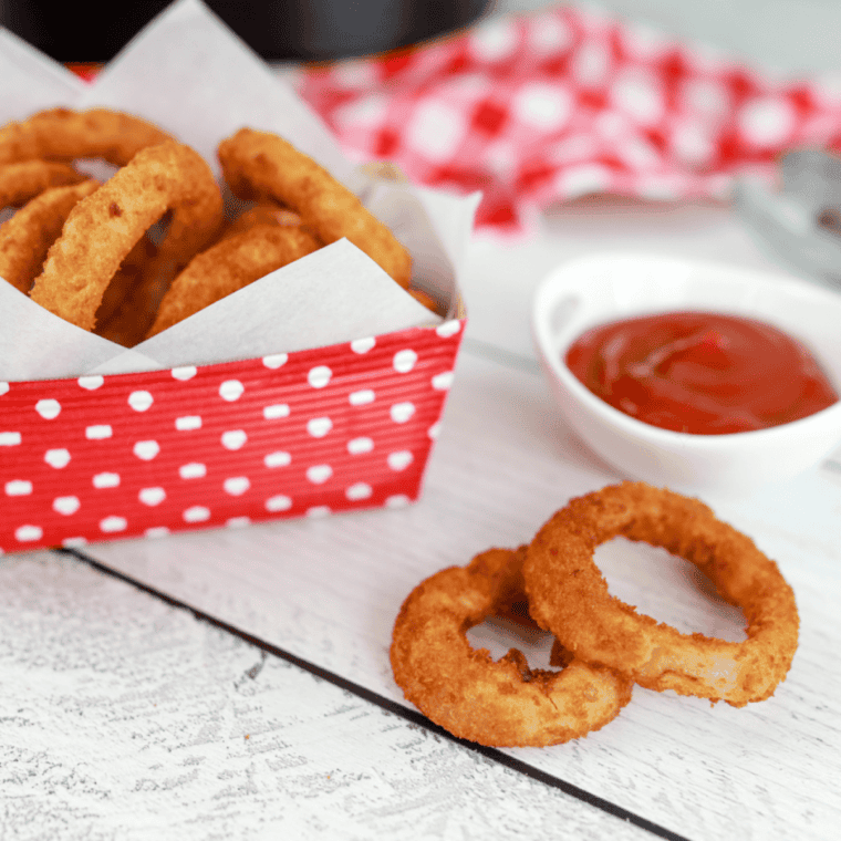 Golden Alexia Onion Rings cooked in an air fryer, served on a white plate with a side of dipping sauce.