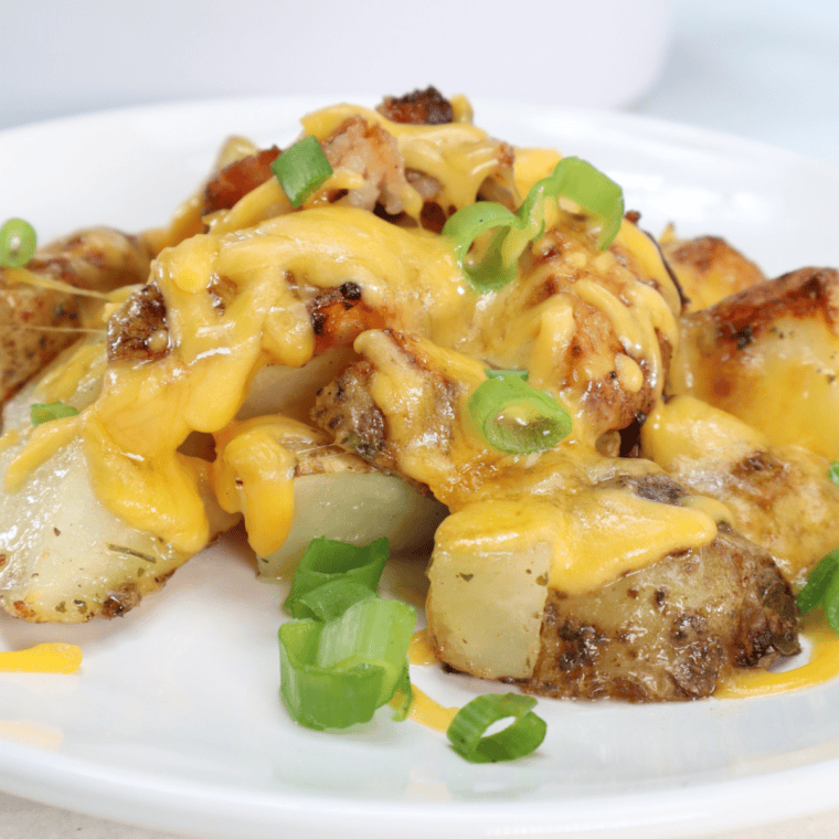 Golden air fryer cheesy ranch potatoes topped with melted cheese and sprinkled with herbs, served in a white bowl
