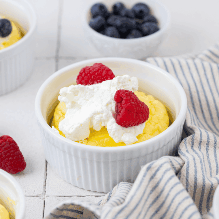 Golden, fluffy air fryer souffl&eacute; pancakes in ramekins topped with whipped cream and fresh berries.
