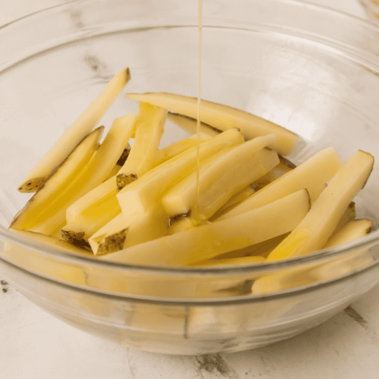 Raw skin-on potato sticks soaking in a glass bowl of cold water