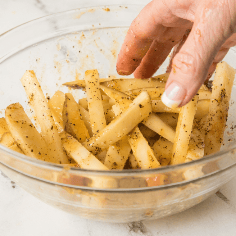 Potato sticks tossed with oil and cornstarch in a mixing bowl, evenly coated and chalky-looking