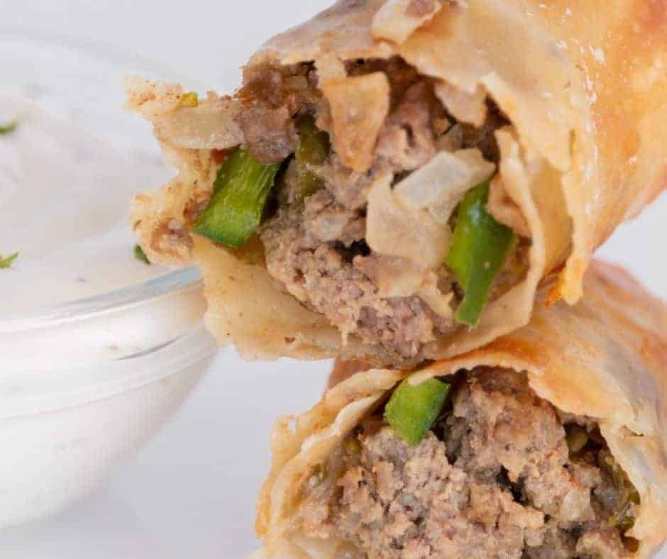 close up: cooked cheesesteak egg rolls next to a white dipping sauce