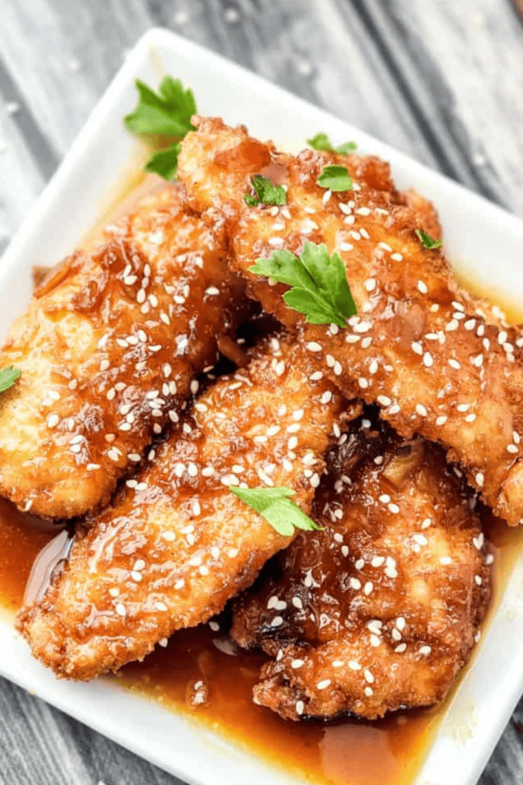 Crispy Copycat Whiskey-Glazed Sesame Chicken Strips coated in a flavorful whiskey glaze, garnished with sesame seeds.