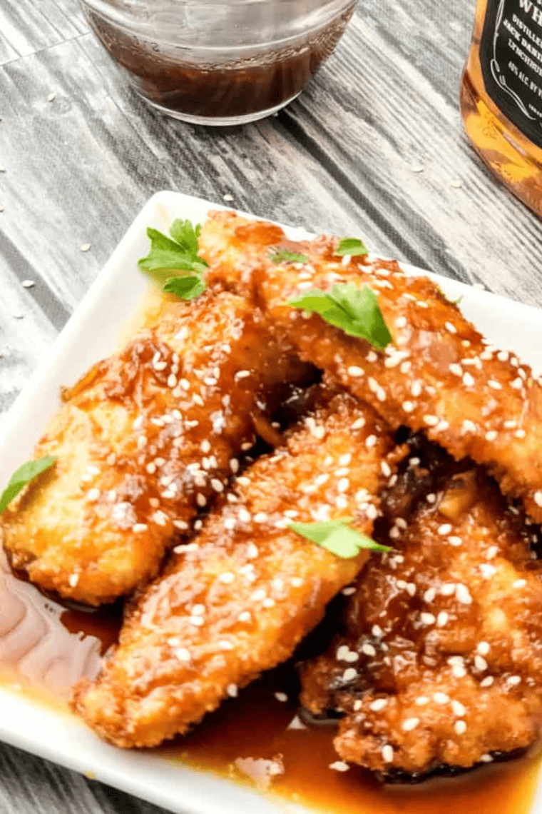 Golden crispy chicken strips coated in a rich, flavorful Jack Daniel’s whiskey glaze, sprinkled with sesame seeds for the perfect touch.