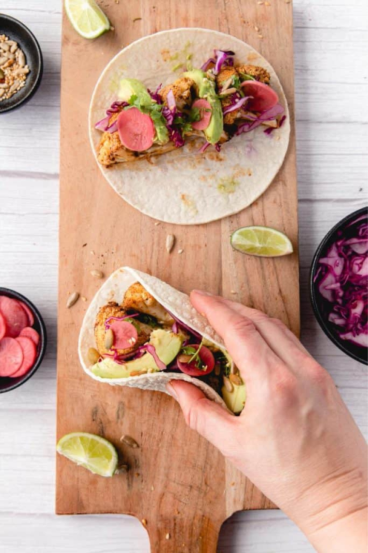 "Garnishing cauliflower tacos with fresh lime wedges and seed mix"