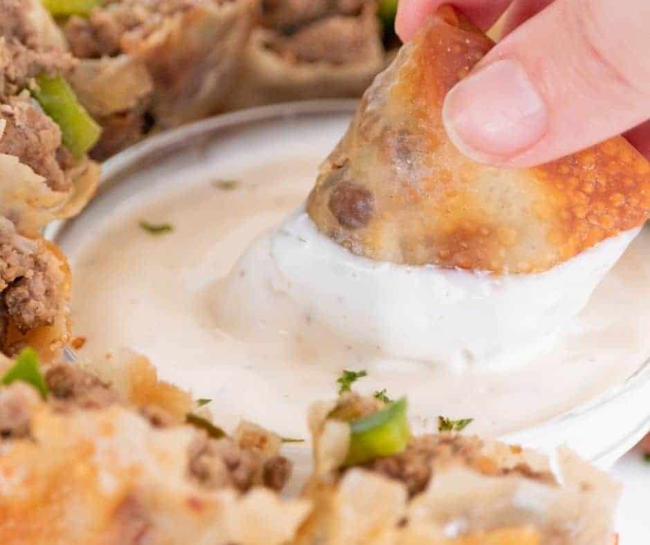 close up: dipping philly cheesesteak egg rolls in a white sauce