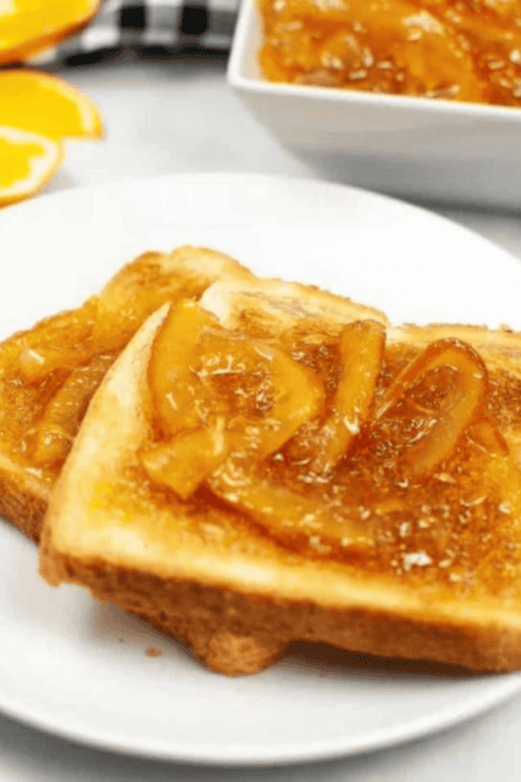 Orange marmalade on buttered sourdough toast with a jar of marmalade in the background