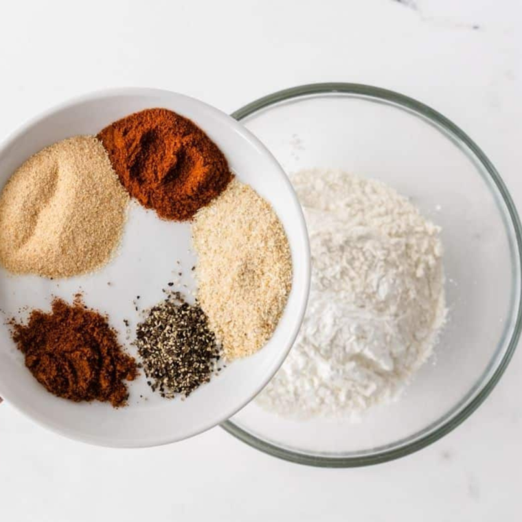 Mixing flour, cornstarch, paprika, garlic powder, onion powder, red pepper, black pepper, and salt to make Cajun spice blend.