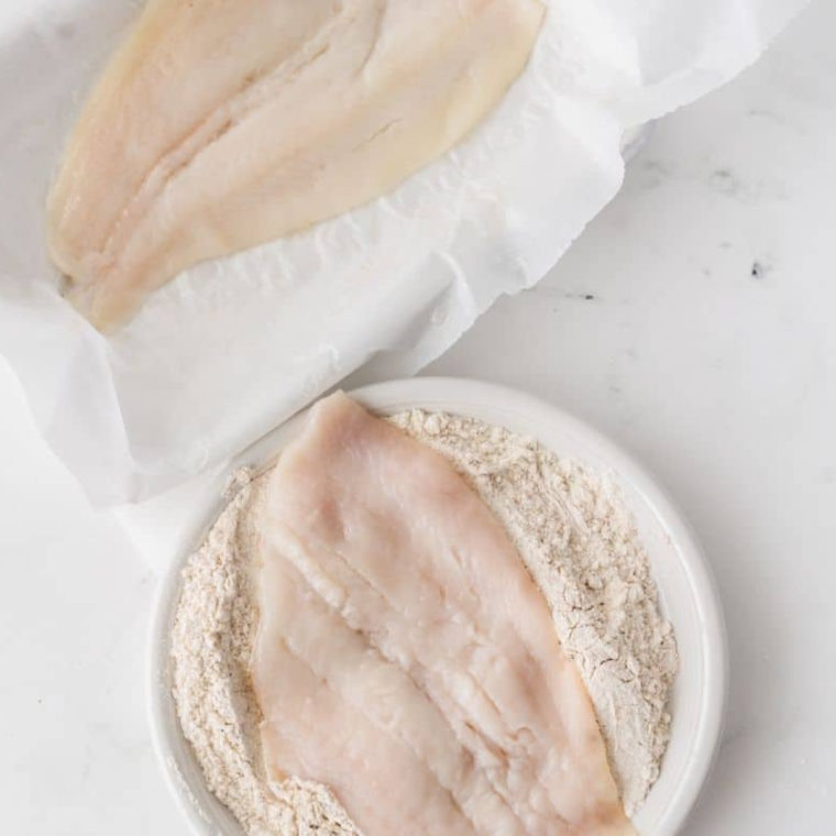 Rubbing olive oil on flounder fillets and coating with Cajun flour mix, pressing firmly to ensure coating sticks.