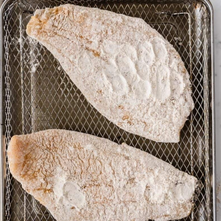 Spraying air fryer basket and coated flounder fillets with cooking spray, then air frying at 400°F for golden brown results.