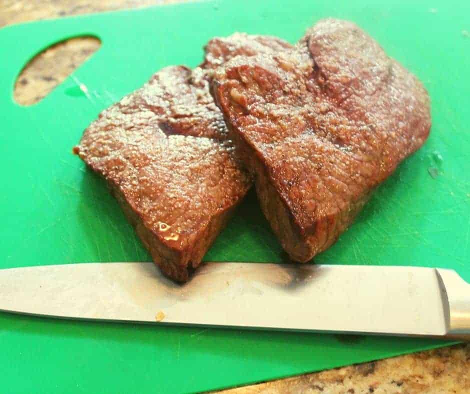 steak in air fryer resting on a green cutting board with a large knife visible