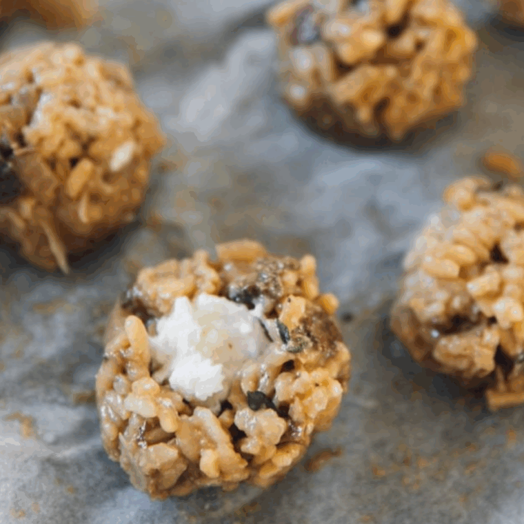 Hands forming risotto into balls with mozzarella centers, arranged on a tray and ready to chill in the fridge.