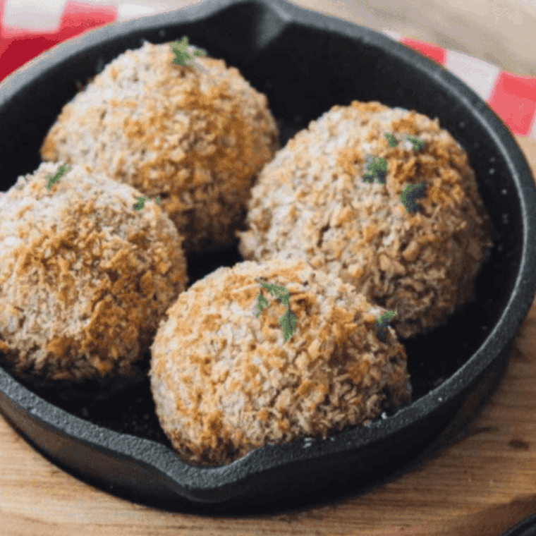 Golden brown arancini rice balls on a plate, one cut open to reveal melted mozzarella inside, air fried to a crispy finish.