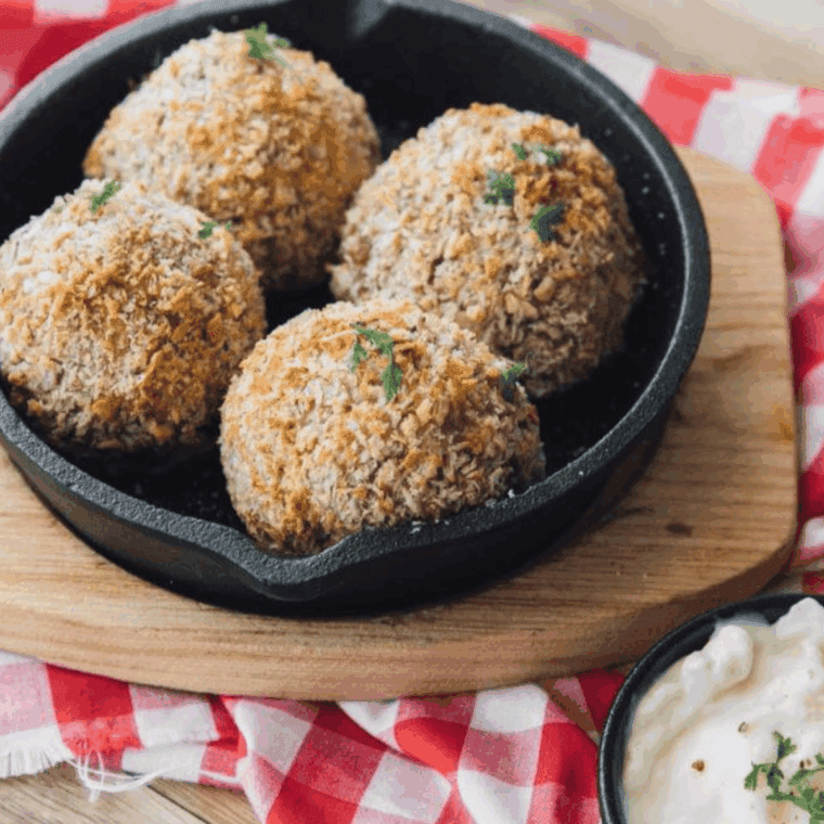 Crispy air fryer arancini rice balls stacked on a plate with gooey cheese oozing from the center.