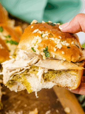 "Pulling apart cheesy chicken pesto sliders with melted mozzarella and green pesto on toasted golden-brown rolls."