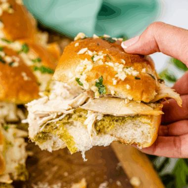 "Pulling apart cheesy chicken pesto sliders with melted mozzarella and green pesto on toasted golden-brown rolls."