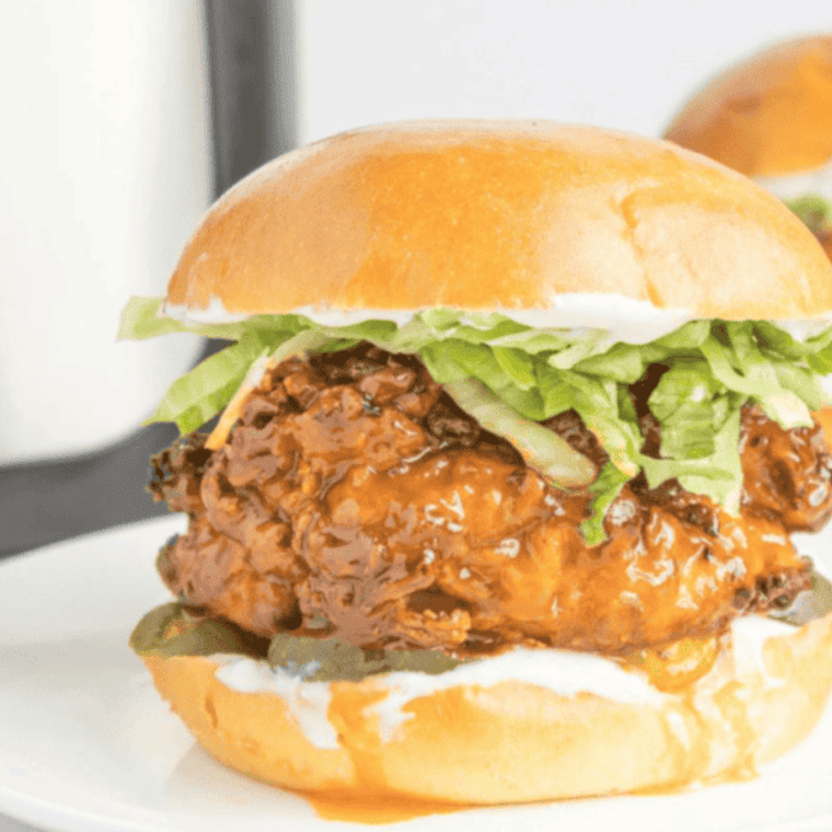 A crispy Air Fryer Hot Honey Chicken Sandwich served on a toasted bun with lettuce, pickles, and a drizzle of hot honey, plated alongside golden fries.