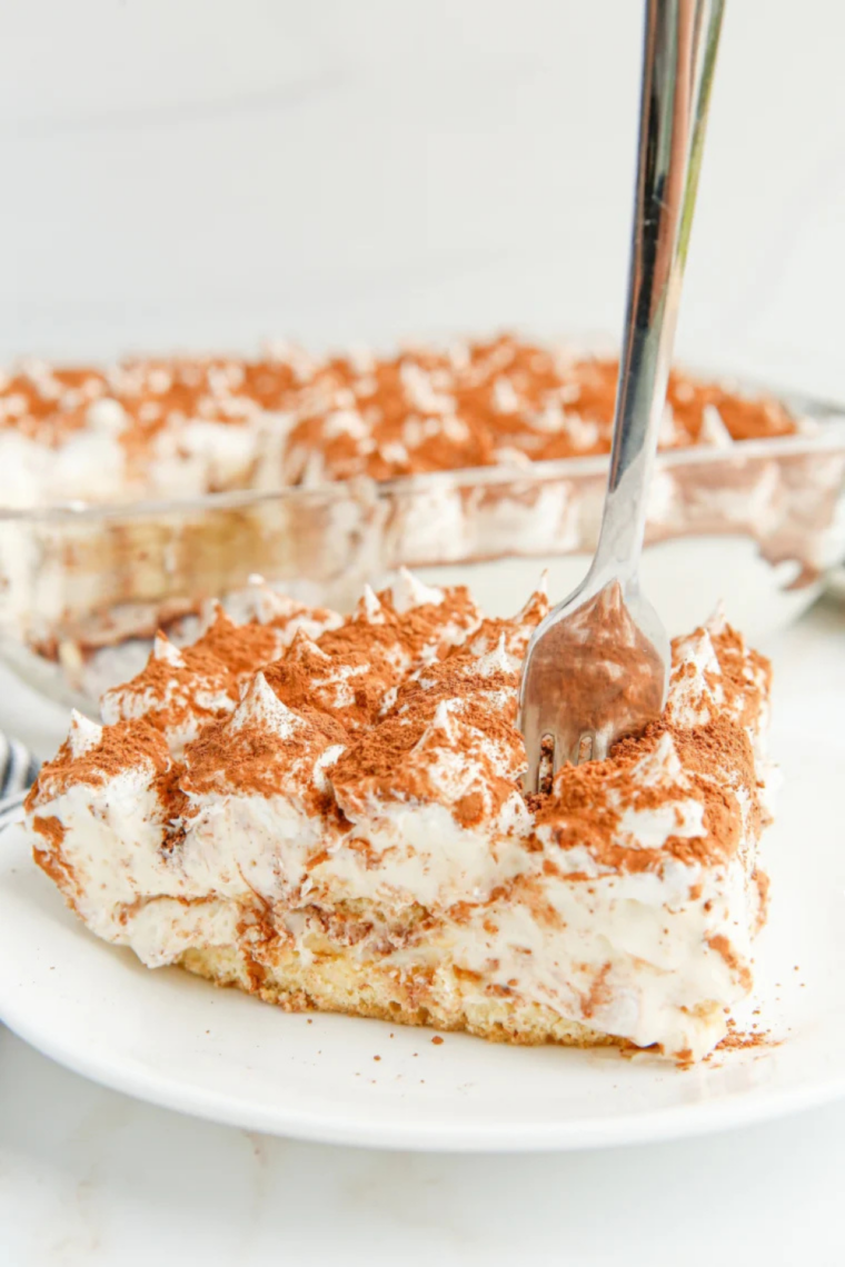Fork lifting a bite from a slice of air fryer tiramisu, revealing distinct ladyfinger and mascarpone layers