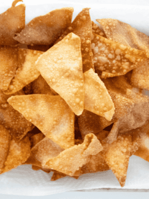 Crispy golden air fryer wonton chips piled in a white bowl with a small dish of dipping sauce (recommended)
