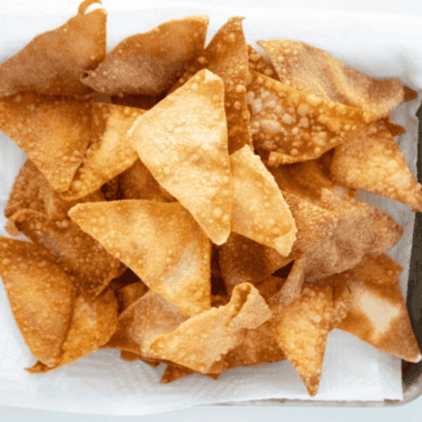 Crispy golden air fryer wonton chips piled in a white bowl with a small dish of dipping sauce (recommended)