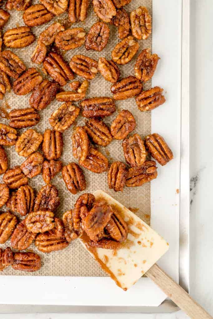 overhead: baking sheet of candied pecans with a spatula
