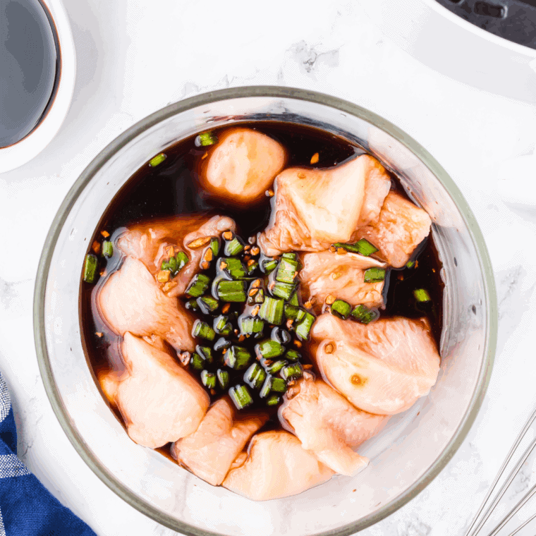 Chicken pieces soaking in teriyaki marinade in a bowl, covered and ready to refrigerate.