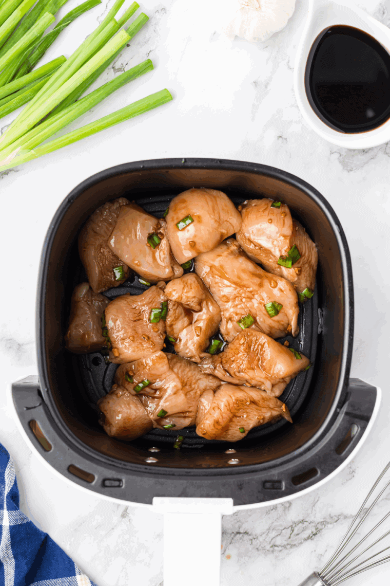 Chicken thighs and breasts placed in an air fryer basket, brushed with oil, cooking until golden brown and fully cooked.