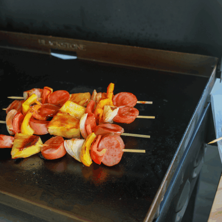 Juicy kielbasa slices cooking on a hot Blackstone griddle with peppers and onions.