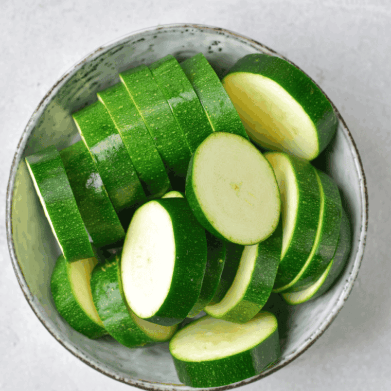 Sliced zucchini rounds on a cutting board, ready for air frying after preheating the air fryer.