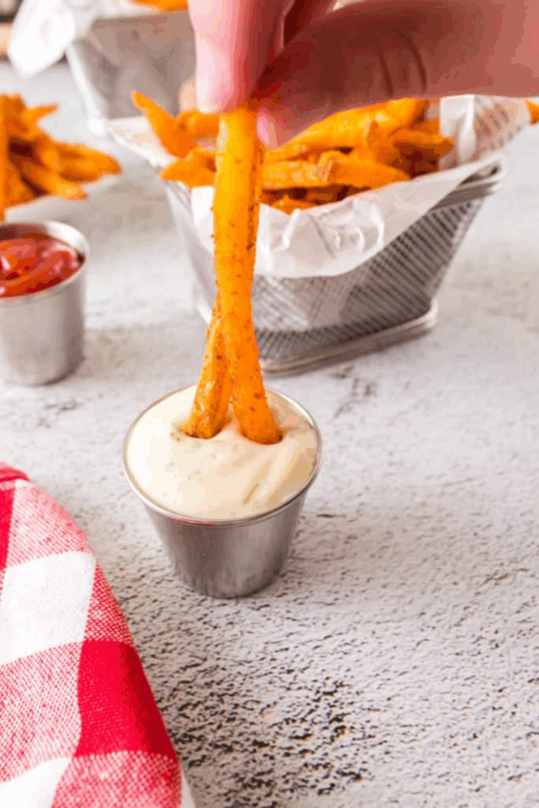 Crispy seasoned fries served in a basket with dipping sauce on the side.