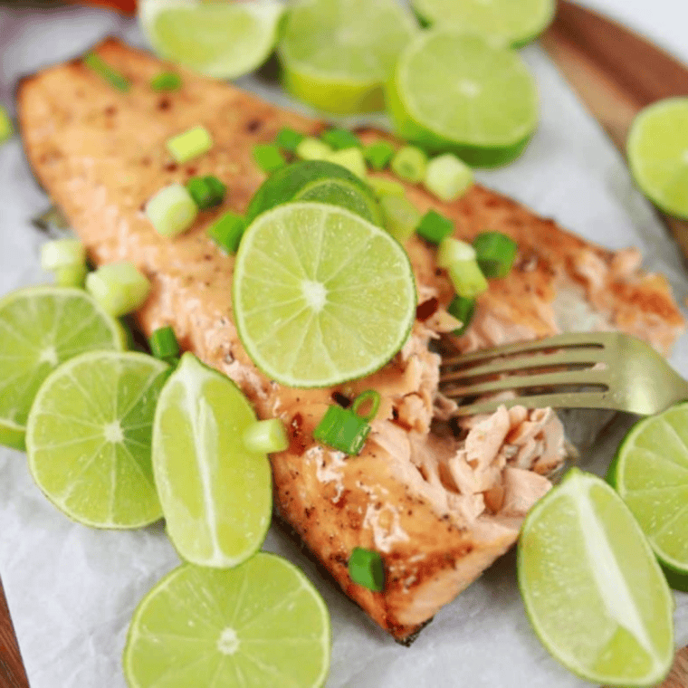 Close-up of perfectly seasoned and flaky Copycat Texas Roadhouse salmon served with fresh lemon slices and a side of vegetables.