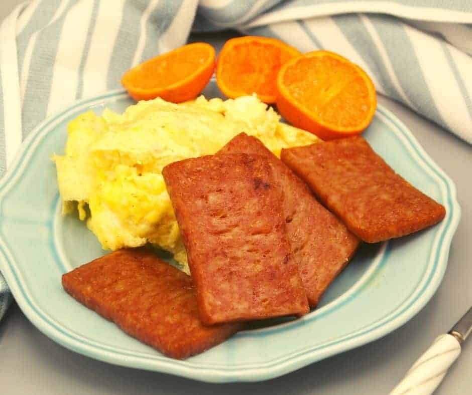 a plate of fried SPAM with scrambled eggs and oranges