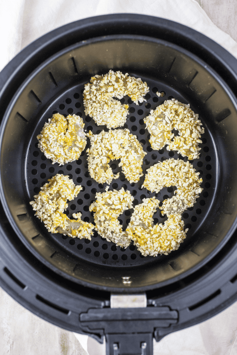 Spraying air fryer basket with oil and arranging shrimp in a single layer.