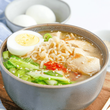 slow cooker chicken ramen in a dark bowl with jammy egg, nori and scallions