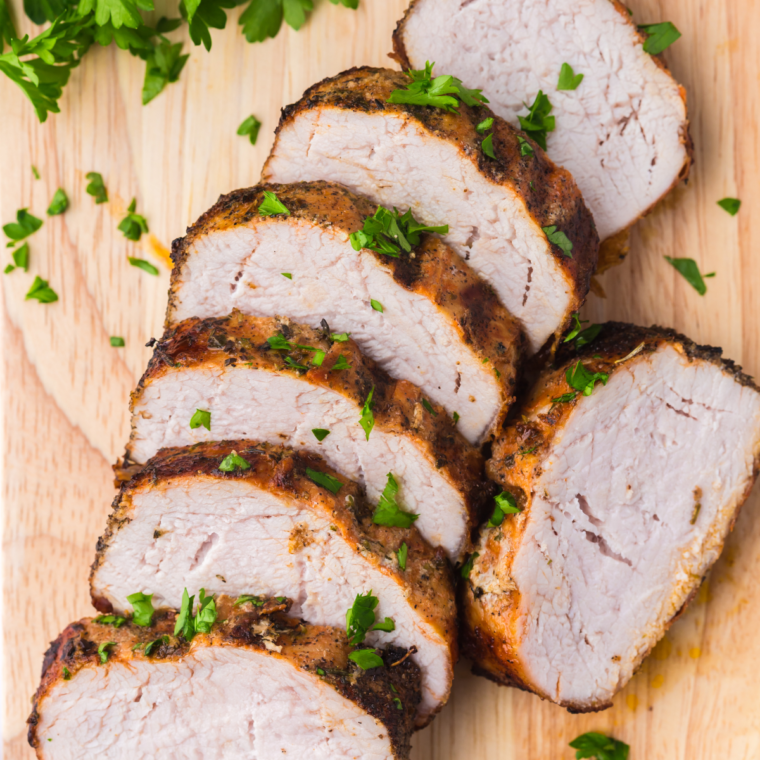 Sliced Traeger smoked pork tenderloin plated with fresh herbs