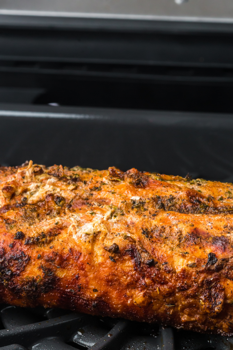 Sliced Traeger smoked pork tenderloin served on a wooden platter with fresh herbs